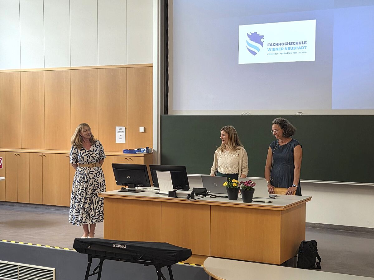 Drei Frauen bei der FH Wiener Neustadt vor einer Leinwand mit dem Logo der Hochschule.